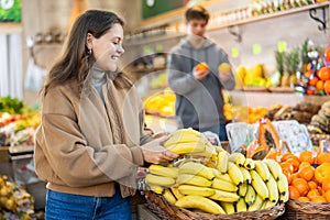 Young woman choosing bananas in vegetable shop