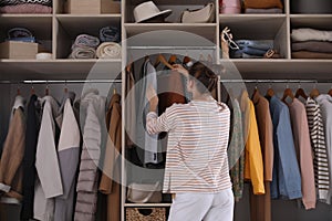 Young woman choosing clothes in wardrobe closet, back view