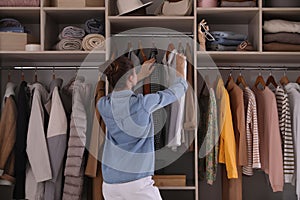 Young woman choosing clothes in wardrobe closet, back view