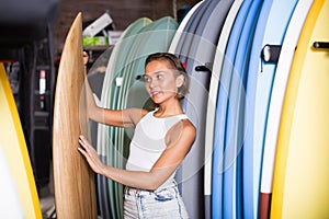 young woman choosing colorful surfboard in the modern shop