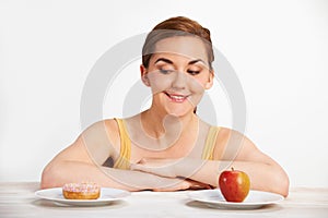 Young Woman Choosing Between Doughnut And Cake For Snack