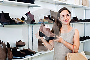 Young woman choosing fall boots in shoes store