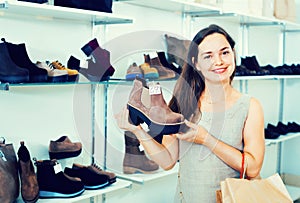 Young woman choosing fall boots in shoes store