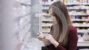 Young woman choosing yogurt in fridge at grocery department of shopping mall.