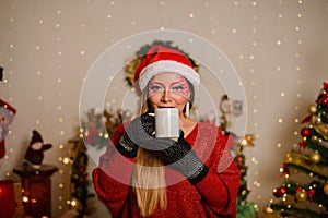 Young woman with Christmas fantasy makeup holding white mug. Selective focus on the mug.