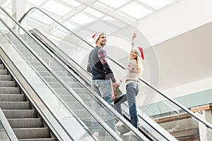 young woman in christmas hat with raised arms looking at camera while her boyfriend