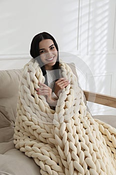 Young woman with chunky knit blanket on sofa at home