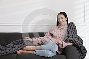 Young woman with chunky knit blanket on sofa at home