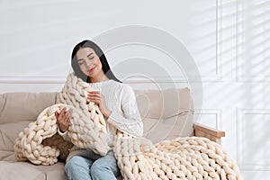 Young woman with chunky knit blanket on sofa at home