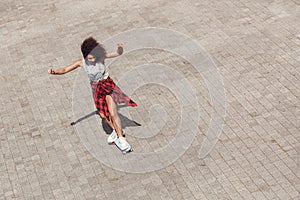 Young woman in the city street riding penny board hands up cheerful top view