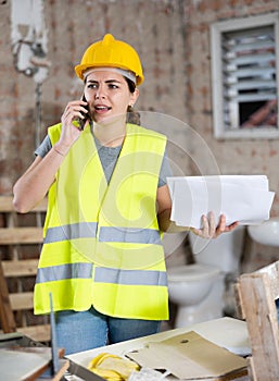 Young woman civil engineer with papers talking on phone at construction site