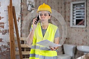 Young woman civil engineer with papers talking on phone at construction site