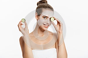 Young woman with clay facial mask holding cucumber slices isolated on white background