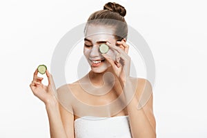 Young woman with clay facial mask holding cucumber slices isolated on white background