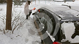 Young woman clean car after snow storm with scraper