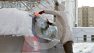 Young woman clean car after snow storm with scraper