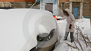 Young woman clean car after snow storm with scraper