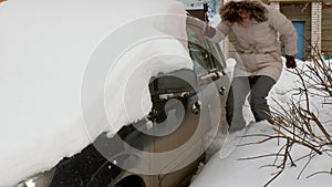 Young woman clean car after snow storm with scraper
