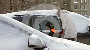 Young woman clean car after snow storm with scraper