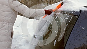 Young woman clean car after snow storm with scraper