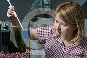 Young woman cleaning aquarium with beta fish at home.