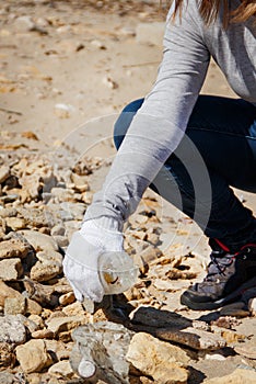 Young woman cleaning beach area from plastic bottles