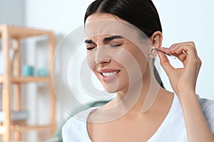 Young woman cleaning ear with cotton swab at home