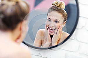 Young woman cleaning face in bathroom mirror