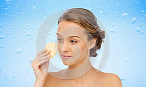 Young woman cleaning face with exfoliating sponge photo