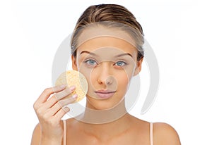 Young woman cleaning face with exfoliating sponge photo