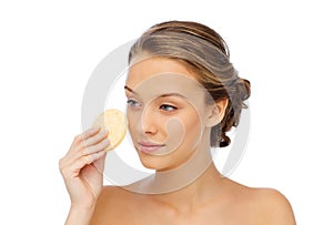 Young woman cleaning face with exfoliating sponge photo