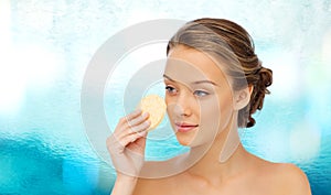 Young woman cleaning face with exfoliating sponge photo
