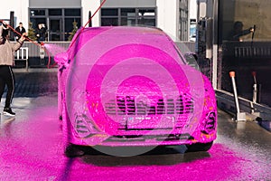 Young woman cleaning her car on self service car wash. Female spread soap using jet sprayer. Pink foam on the car
