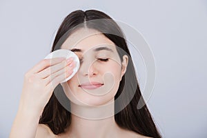 Young woman cleaning her face with cotton pad isolated on white background. Skincare, women`s beauty, hygiene and personal care