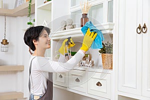 Young woman cleaning her house, she is dusting a shelf, chores and hygiene concept