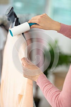 young woman cleaning shirt with lint roller