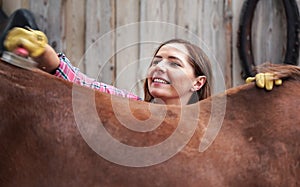 Young woman cleaning horse back with brush, only her face visible from behind the animal