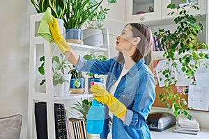 Young woman cleaning house, wearing gloves with cleaning spray and rag