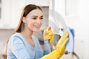 Young woman cleaning kitchen furniture with rag and spray