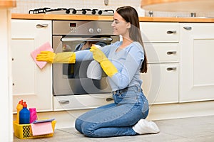 Young woman cleaning kitchen furniture using sprayer