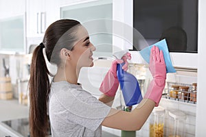 Young woman cleaning microwave oven with rag