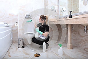 A young woman in a cleaning service uniform lifted the lid of the bathroom toilet. The concept of cleanliness and disinfection in