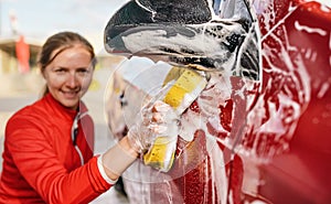 Young woman cleaning side of her car, detail on hand in glove holding yellow sponge