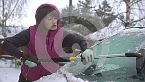 Young woman cleaning Snow and Ice off her Car. Winter snow storm