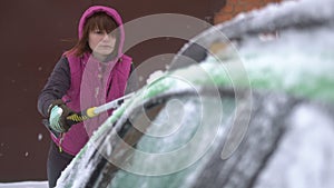 Young woman cleaning Snow and Ice off her Car. Winter snow storm