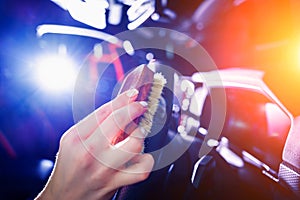 Young woman cleaning the steering wheel of car using a special brush with foam