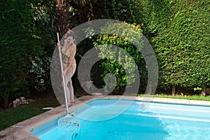 Young woman cleaning swimming pool of fall leaves with cleaning net.