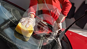 Young woman cleaning windshield of her car, closeup detail on hand in glove holding yellow sponge