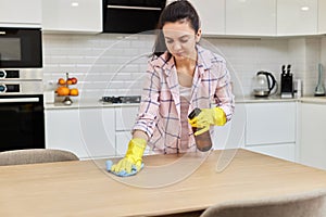 young woman cleaning wooden table with microfiber cloth.