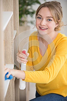 young woman cleaning wooden shelf in living room